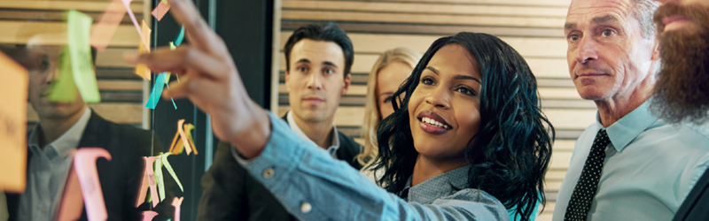 Group of people in front of a board of sticky notes with one woman posting a sticky note to a board